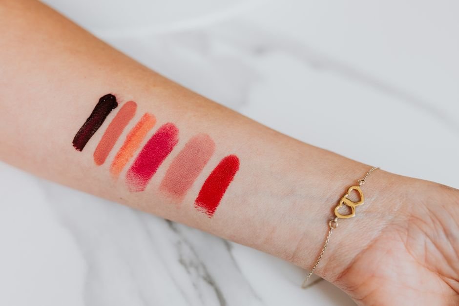 Mulher testando batons MAC Cosmetics em seu braço, mostrando as cores.